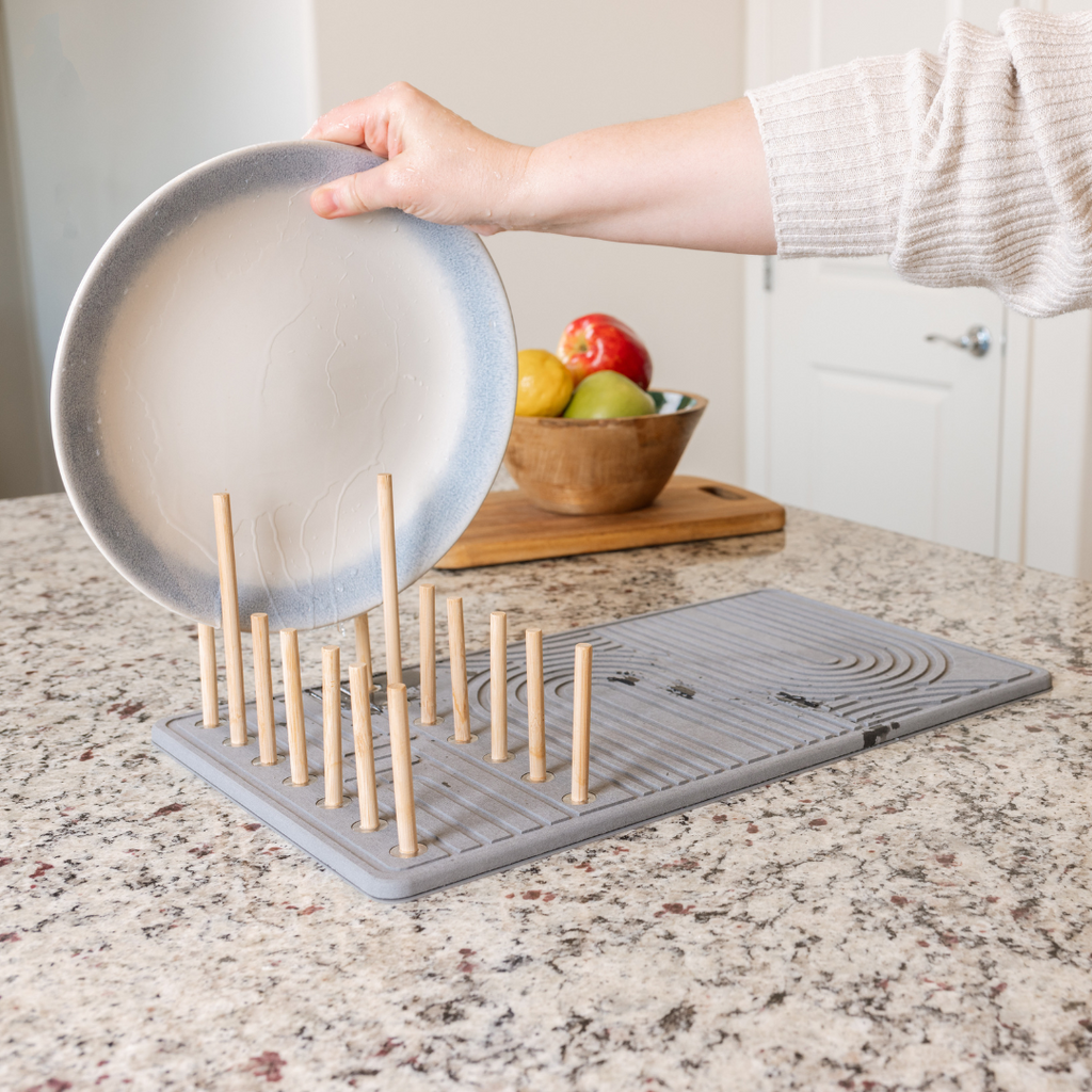 Stone drying mat with built in dish rack and a large plate being placed in the rack.