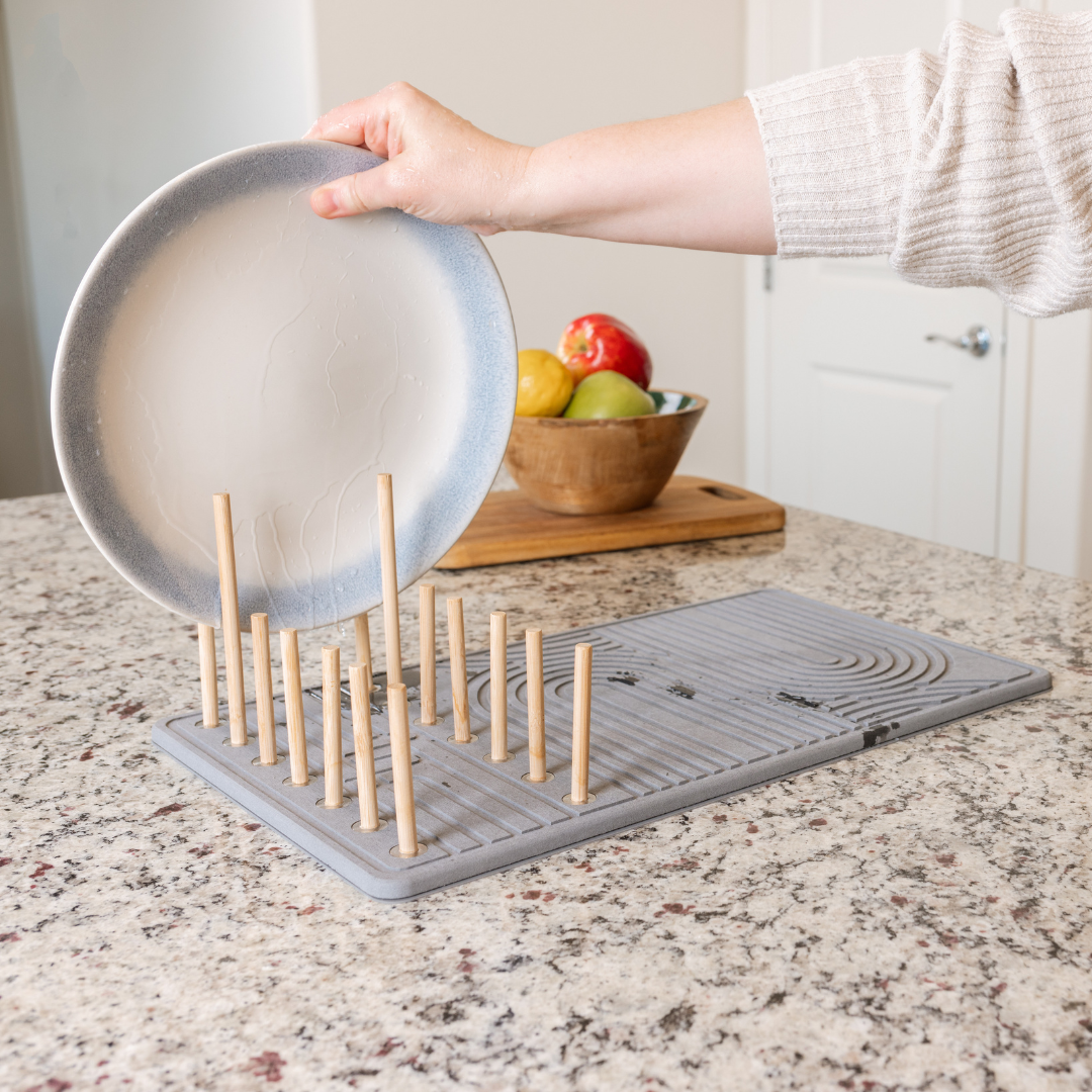 Stone drying mat with built in dish rack and a large plate being placed in the rack.