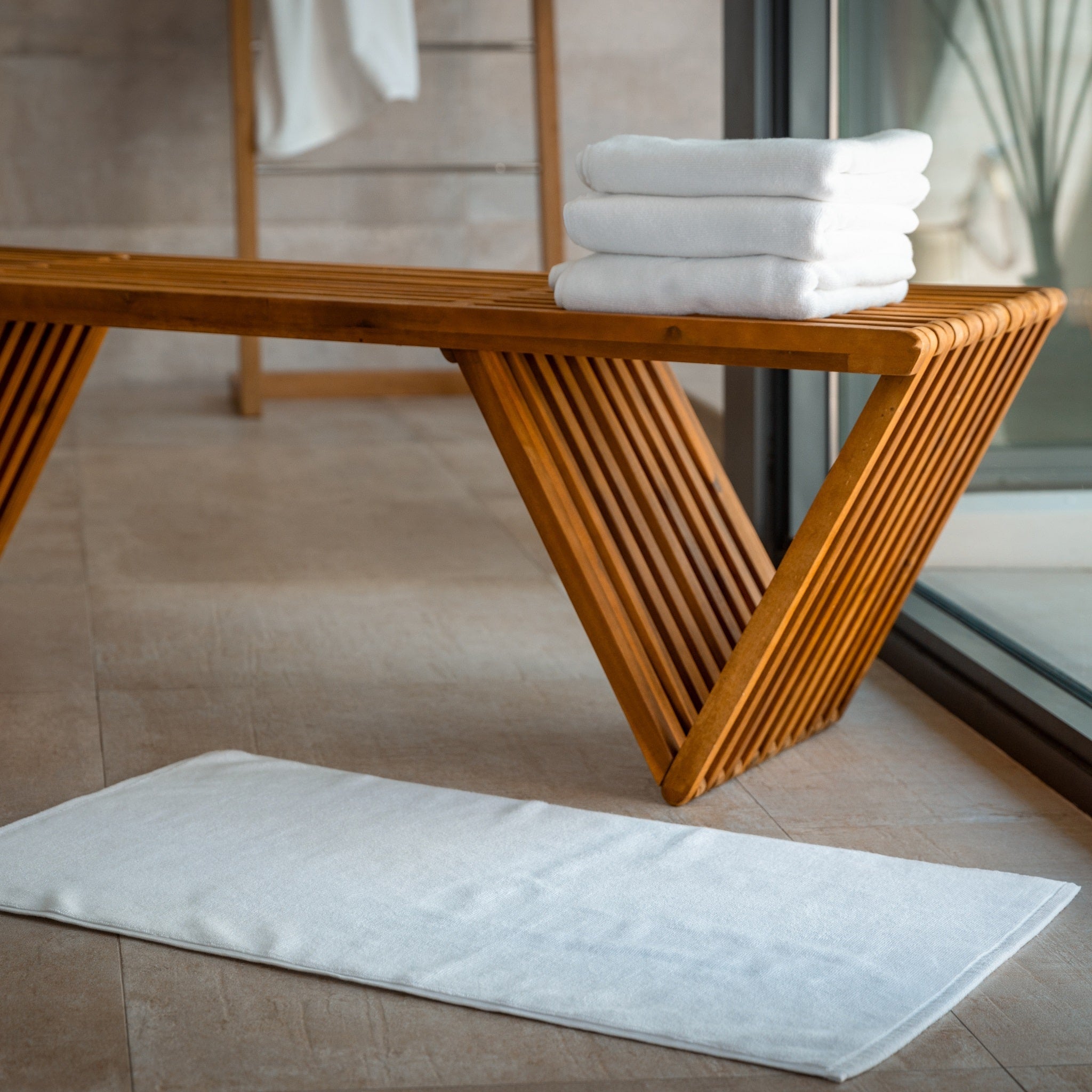 White bath mats stacked on a wooden bench in a bathroom setting