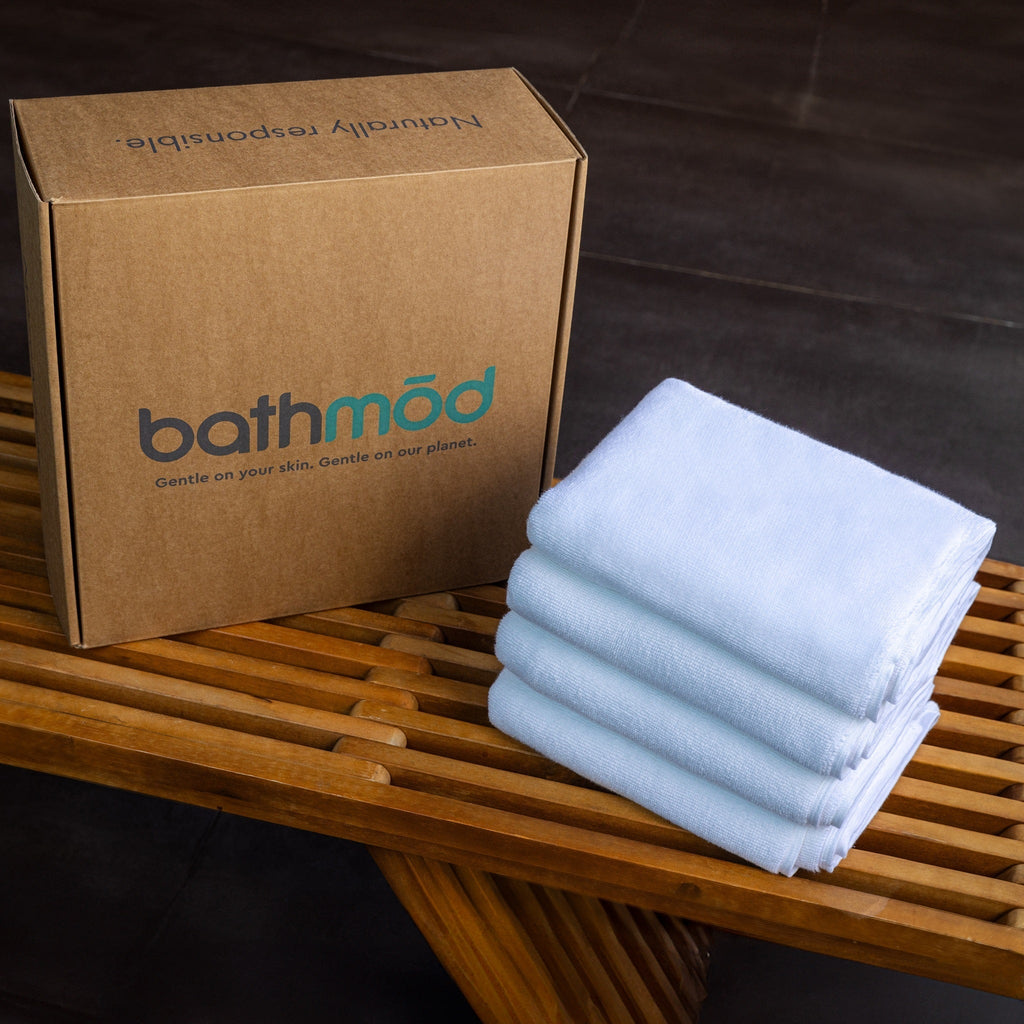 Stack of white bath mats next to a cardboard box with 'bathmod' branding on a wooden surface.