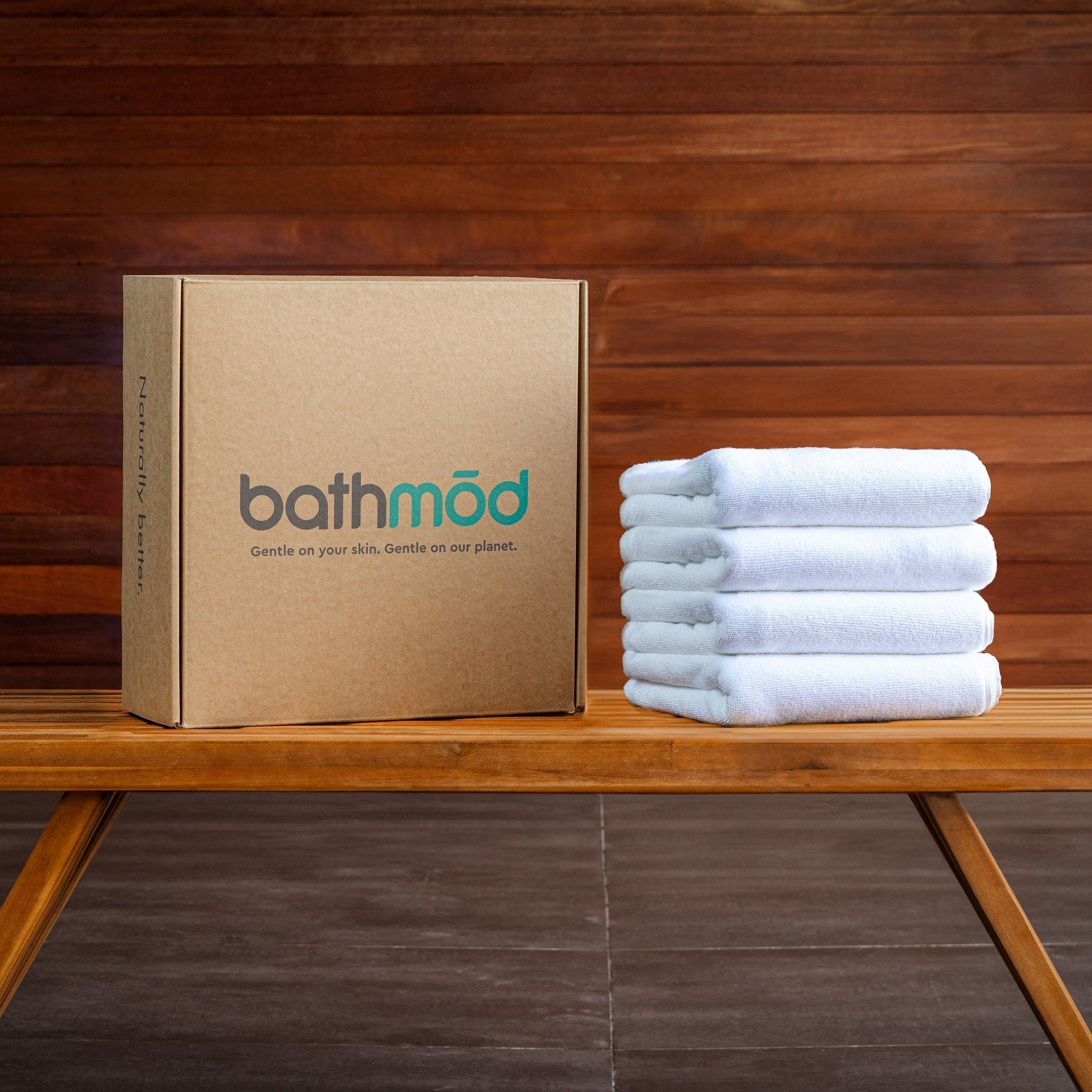 Stack of white bath mats next to a cardboard box with 'bathmöd' branding on a wooden surface.