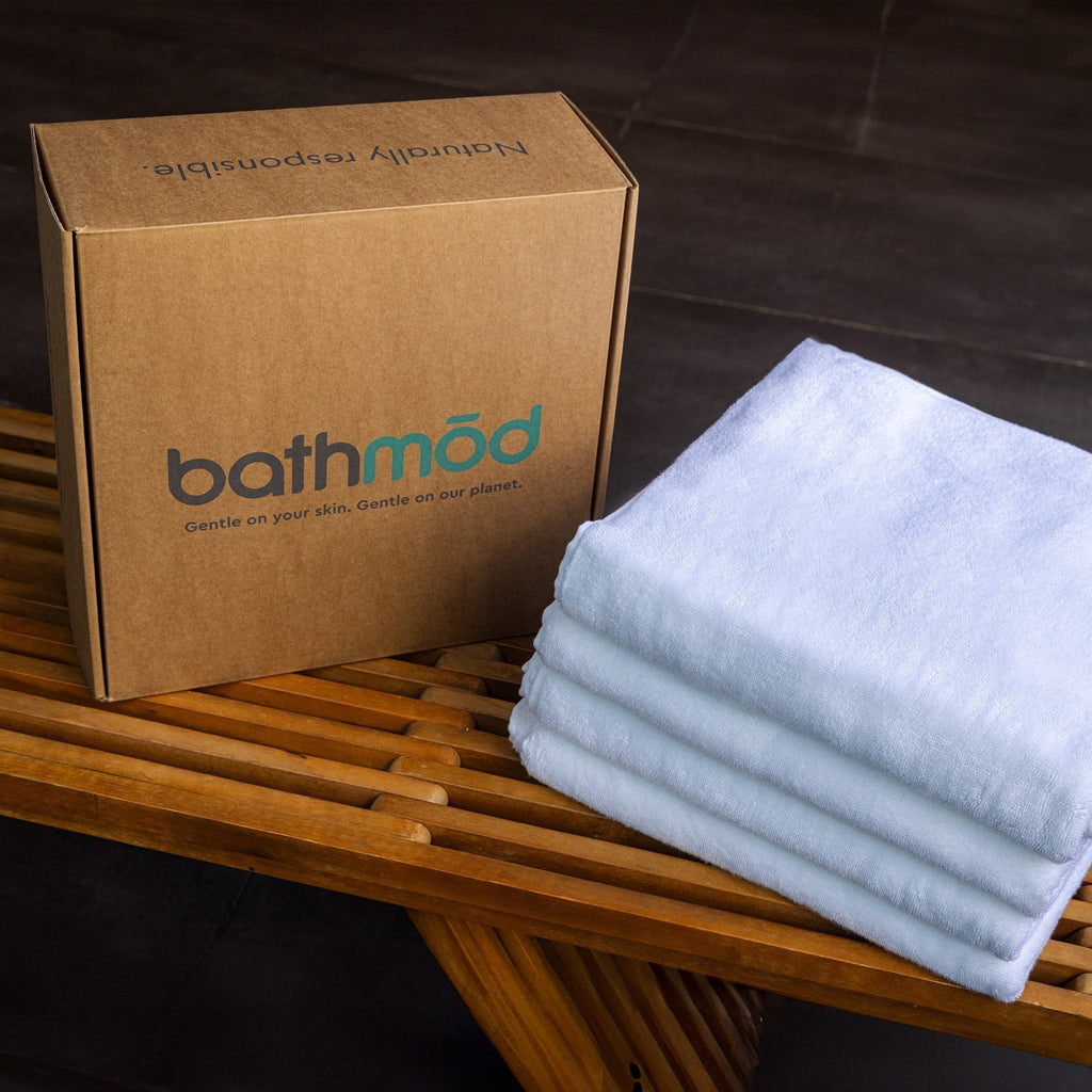 Stack of white towels next to a cardboard box with 'bathmod' branding on a wooden surface.