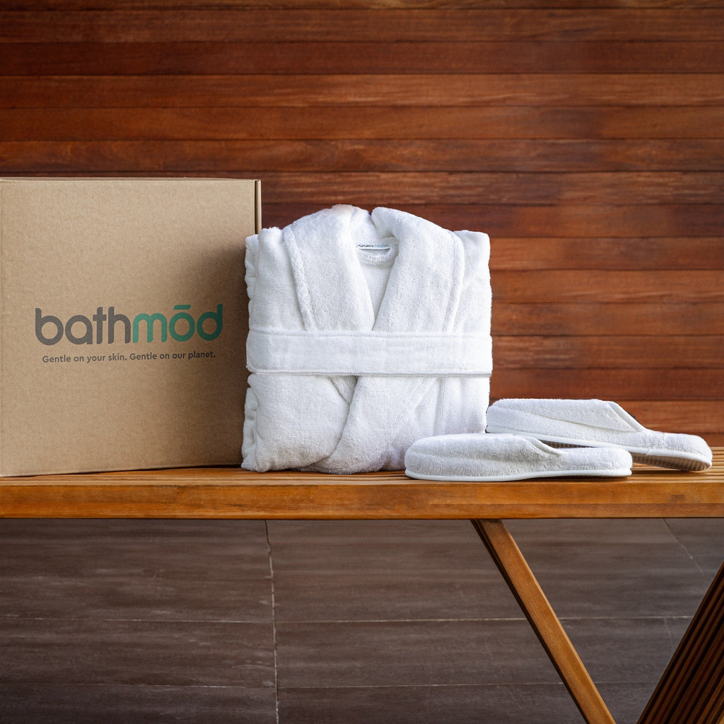 White bathrobe and slippers on a wooden table with a 'bathmōd' box in the background.