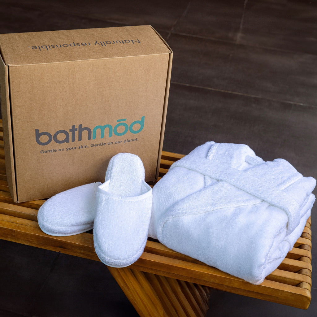 White slippers and folded towel on a wooden tray with bathmod box in the background