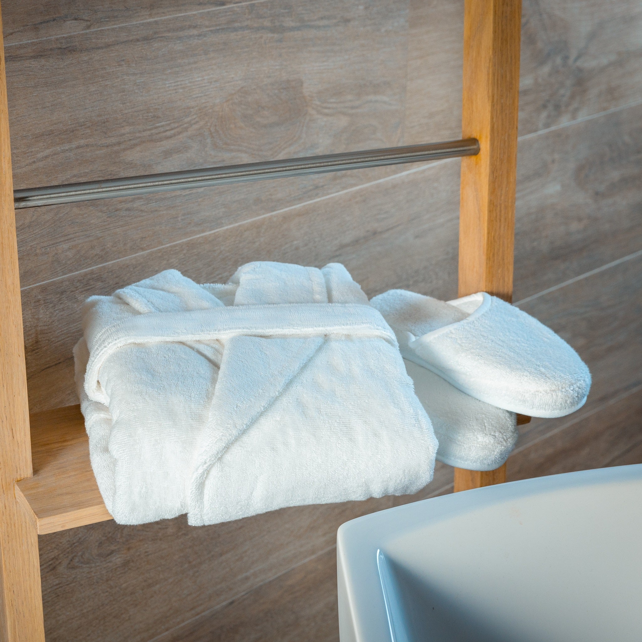 White bathrobe and slippers on a wooden shelf against a tiled wall.