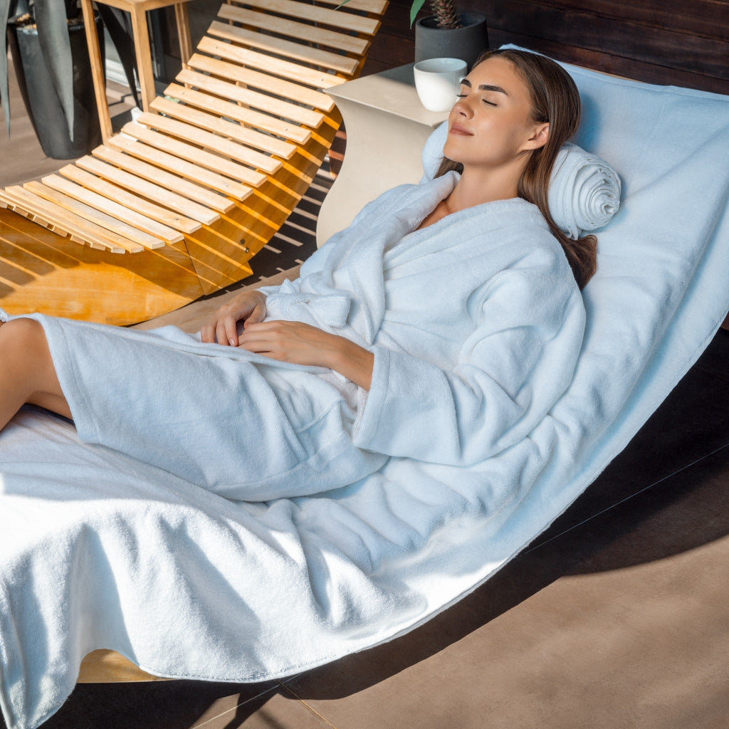 Woman in awhite robe lying on a modern lounge chair with a wooden backrest.
