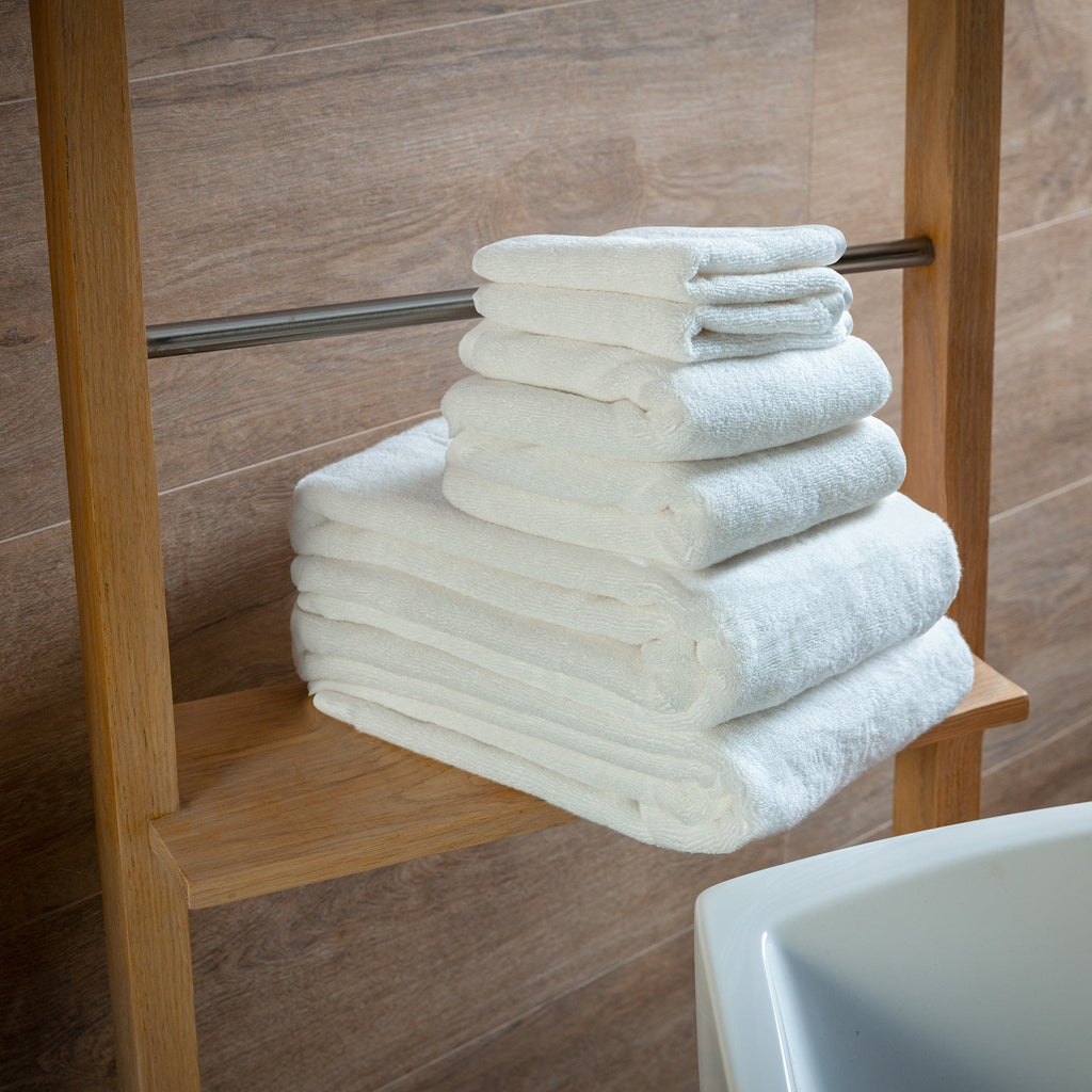 Stack of white towels on a wooden towel rack against a tiled bathroom wall.
