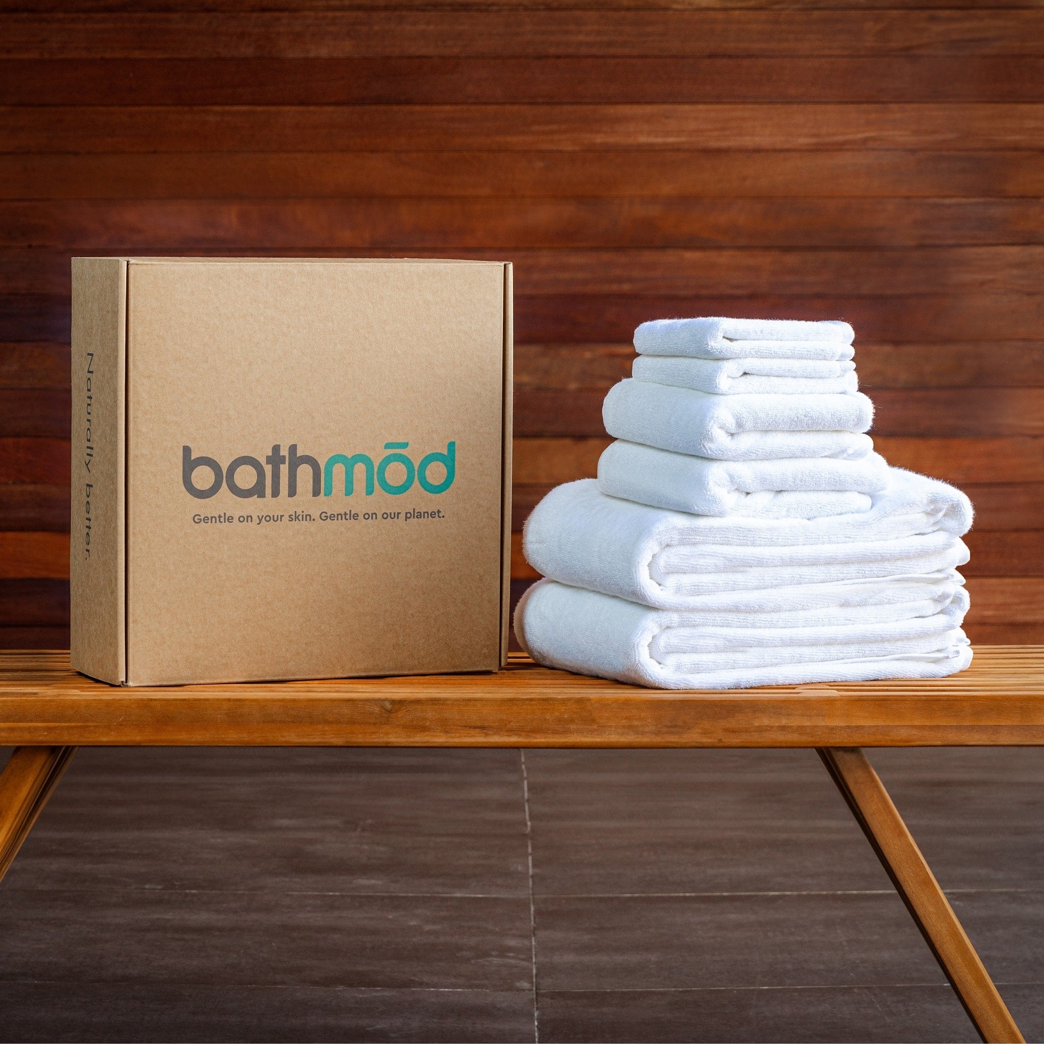 Stack of white towels next to a cardboard box with 'bathmod' branding on a wooden surface.