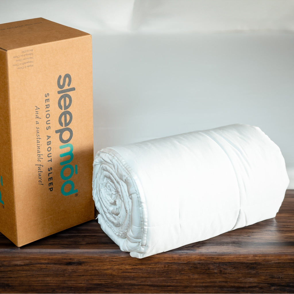 White comforter rolled up next to a cardboard box with Sleepmod.