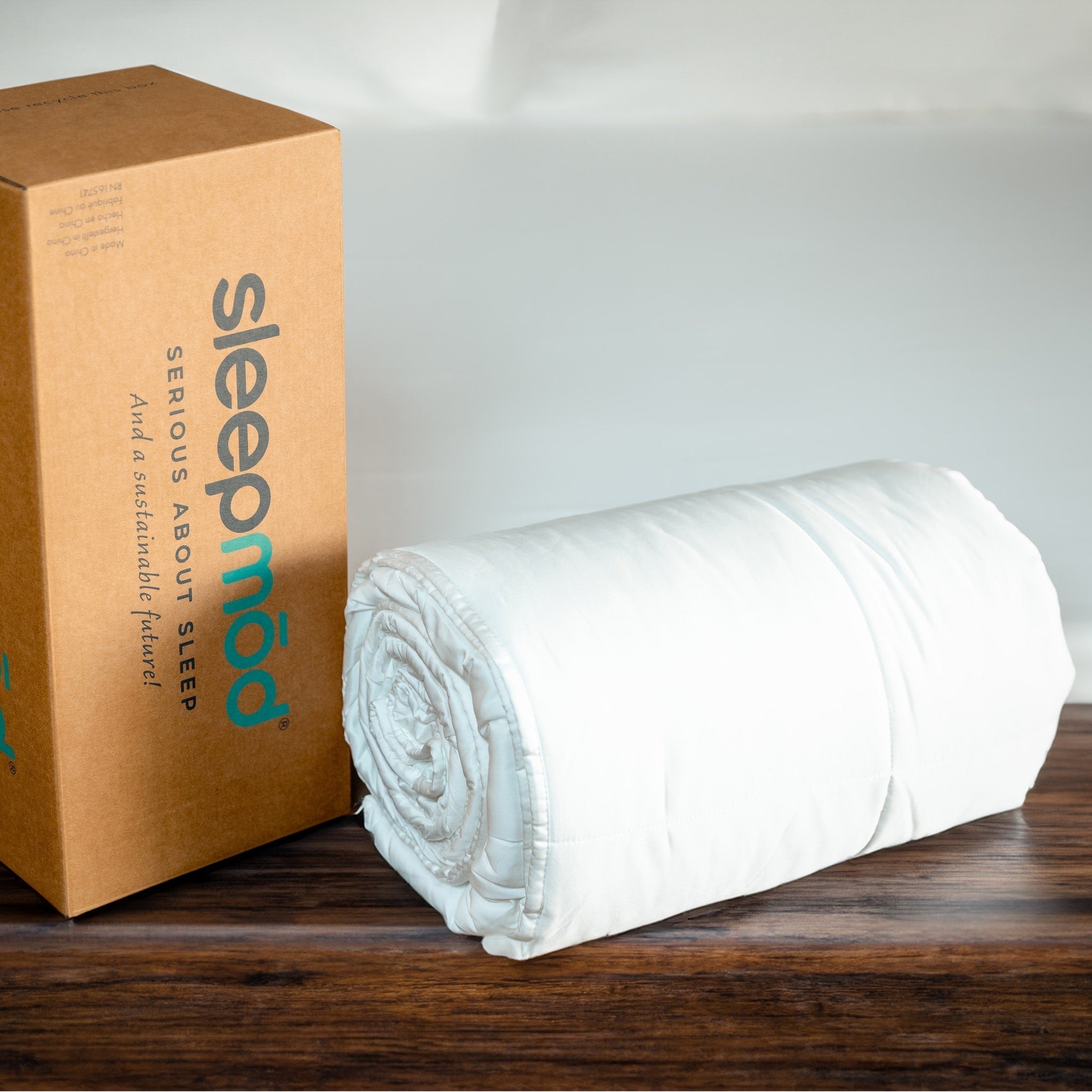 White comforter rolled up next to a cardboard box with Sleepmod.