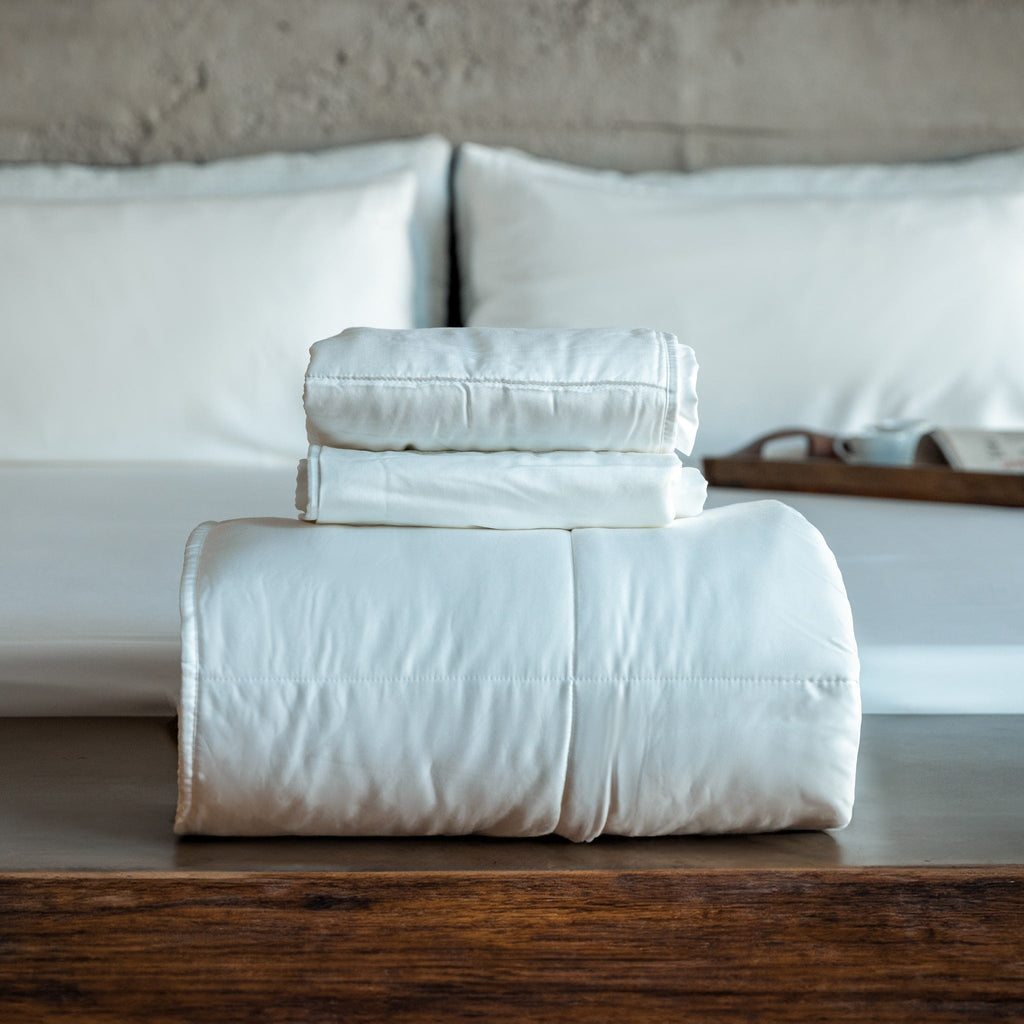 White comforter and 2 shams folded up and sitting on a wood surface.