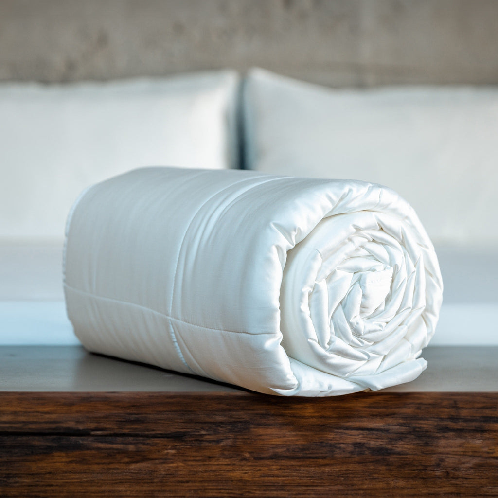 White comforter rolled up sitting on wood surface.