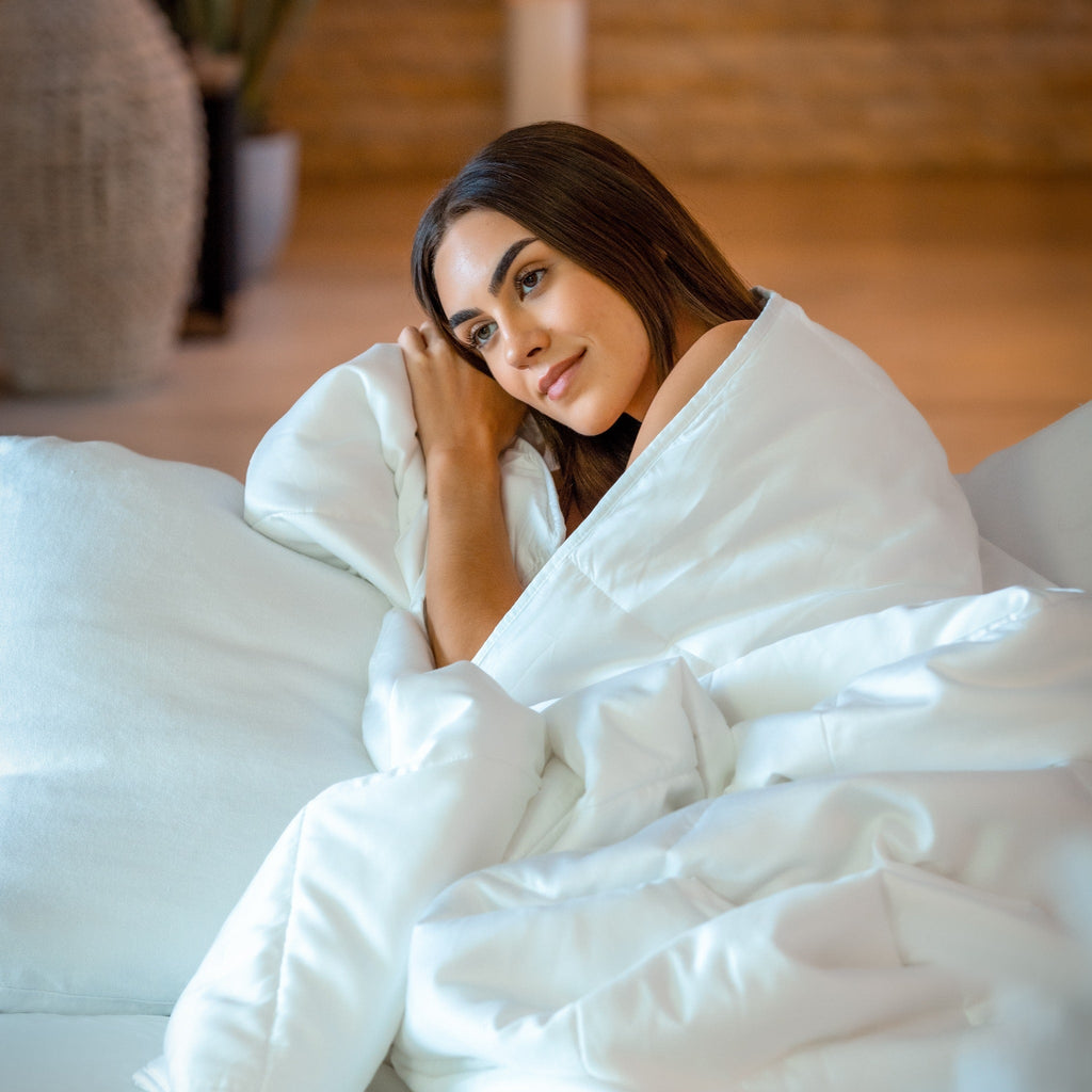 Woman wrapped up in white comforter sitting on bed.