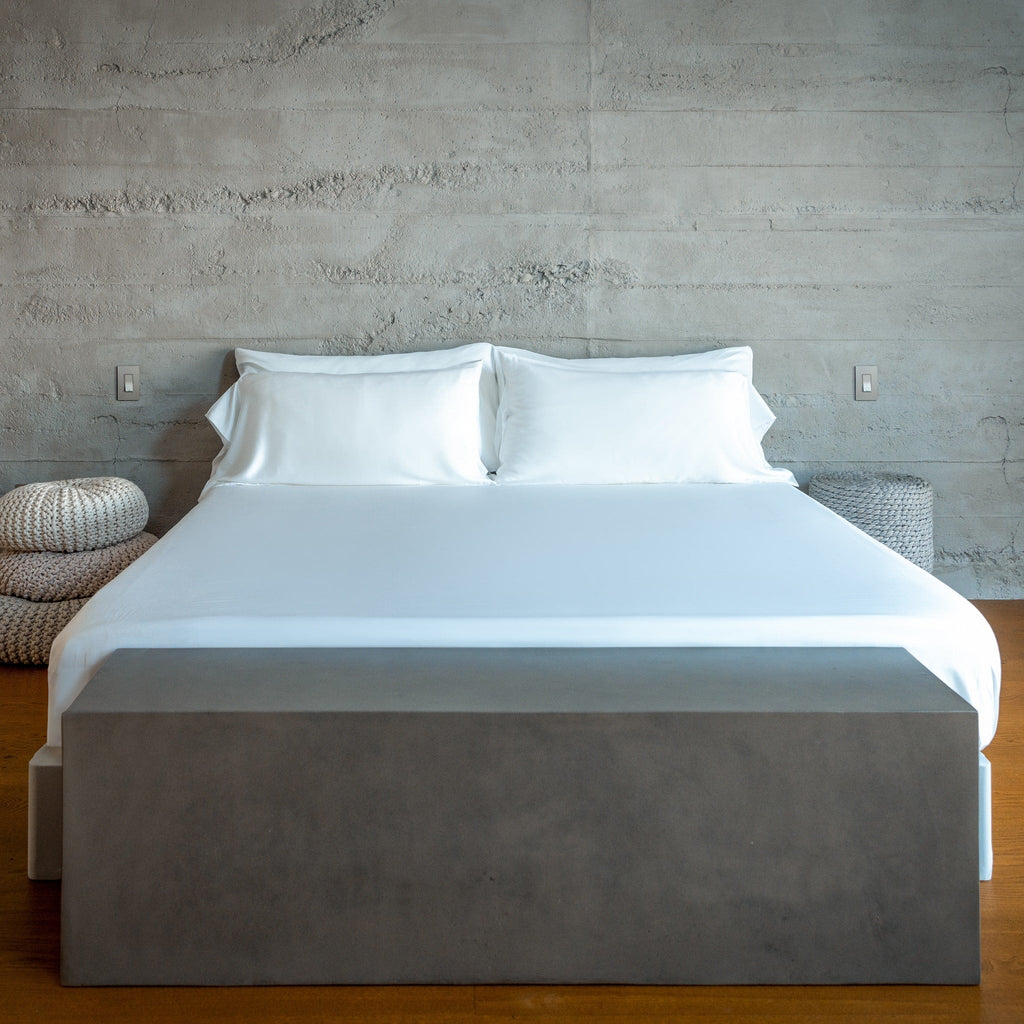Bed with white bedding and gray box spring against a concrete wall.