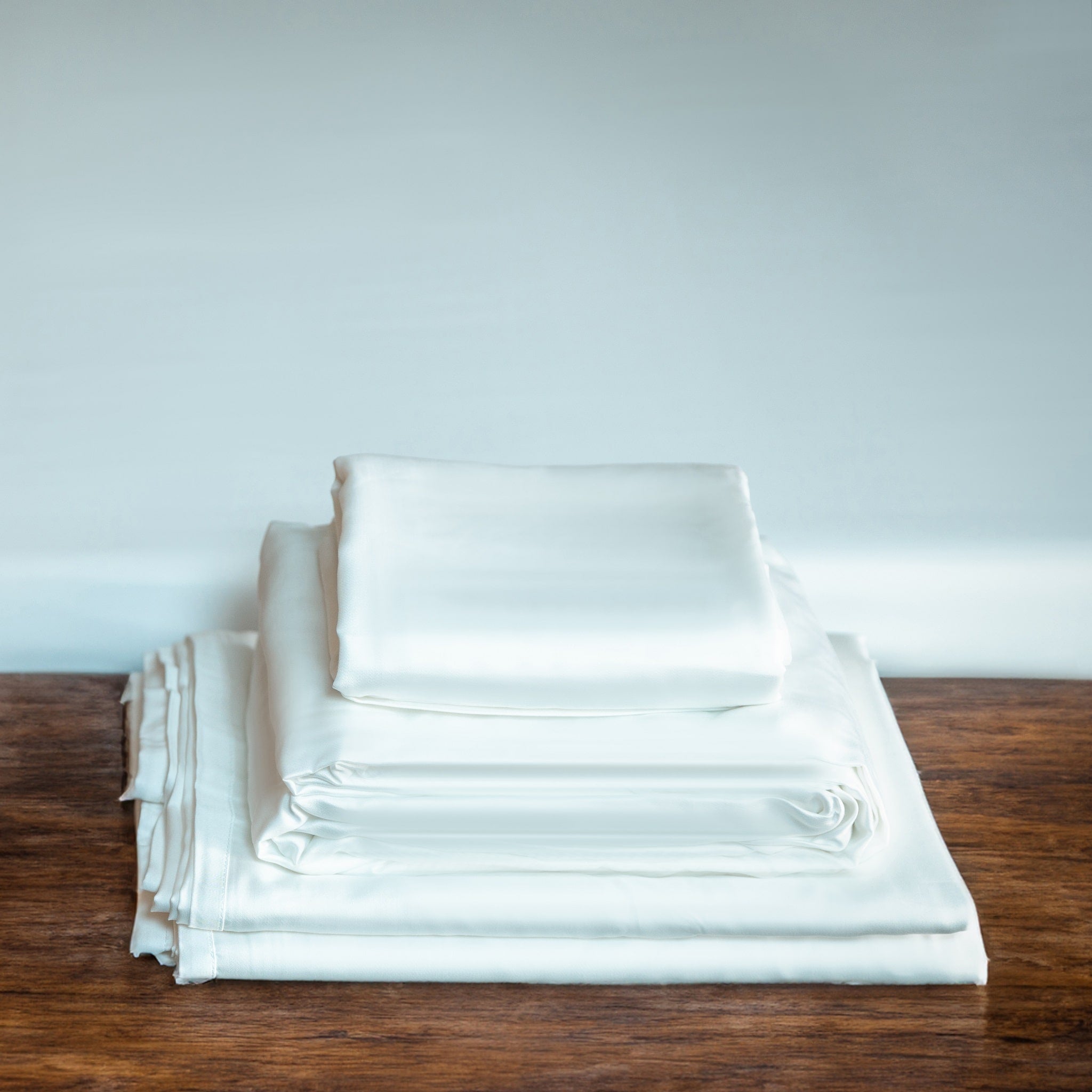 Stack of white folded sheets on a wooden surface with a light gray background