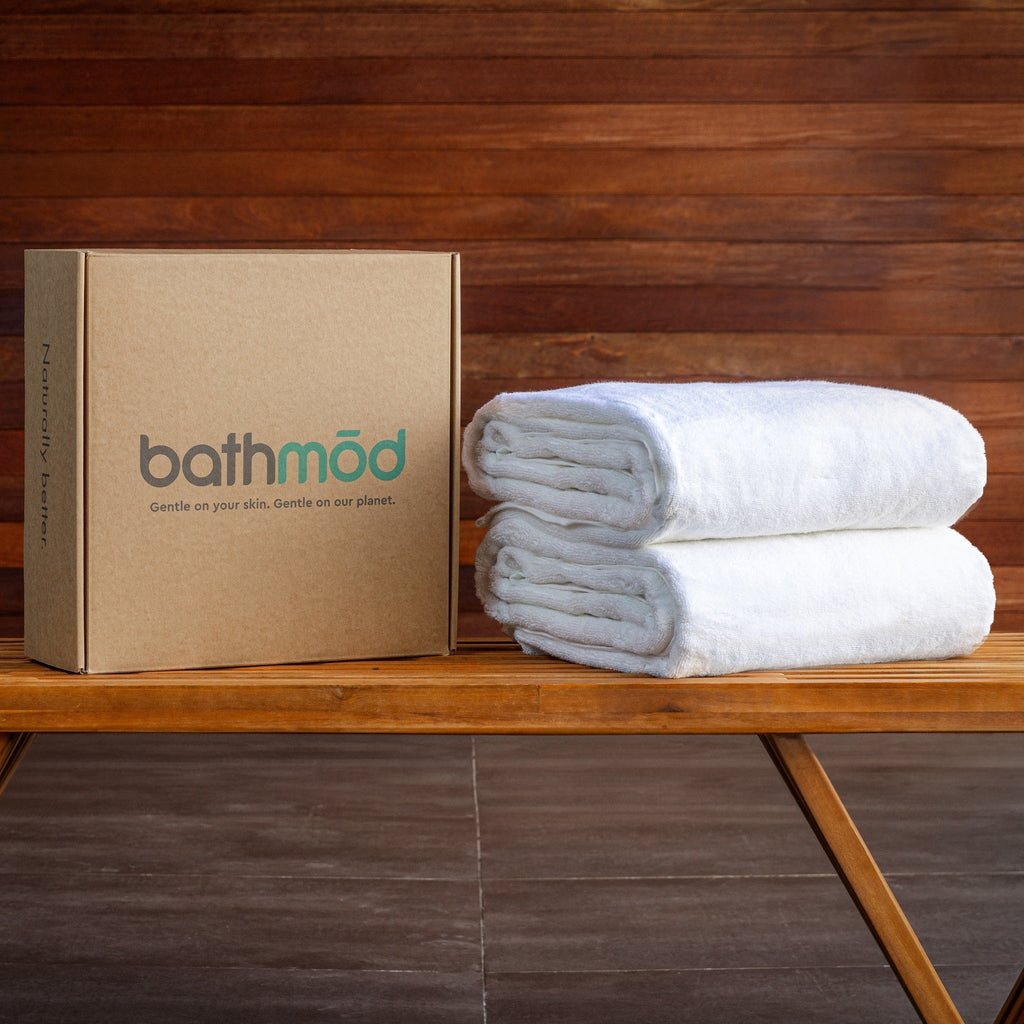Stack of white towels next to a cardboard box with 'bathmöd' branding on a wooden surface.