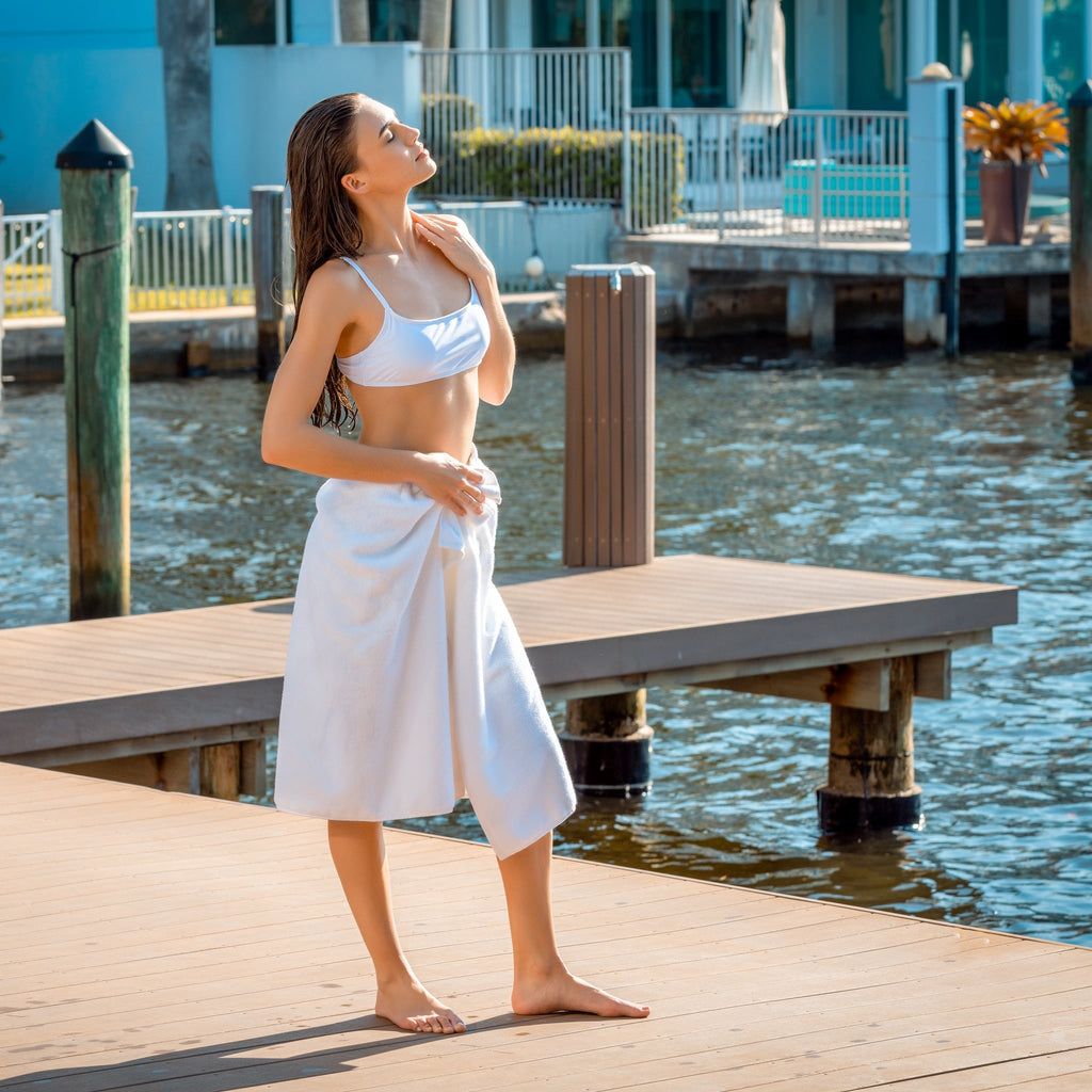 Woman in a white bikini and towel standing on a dock by water