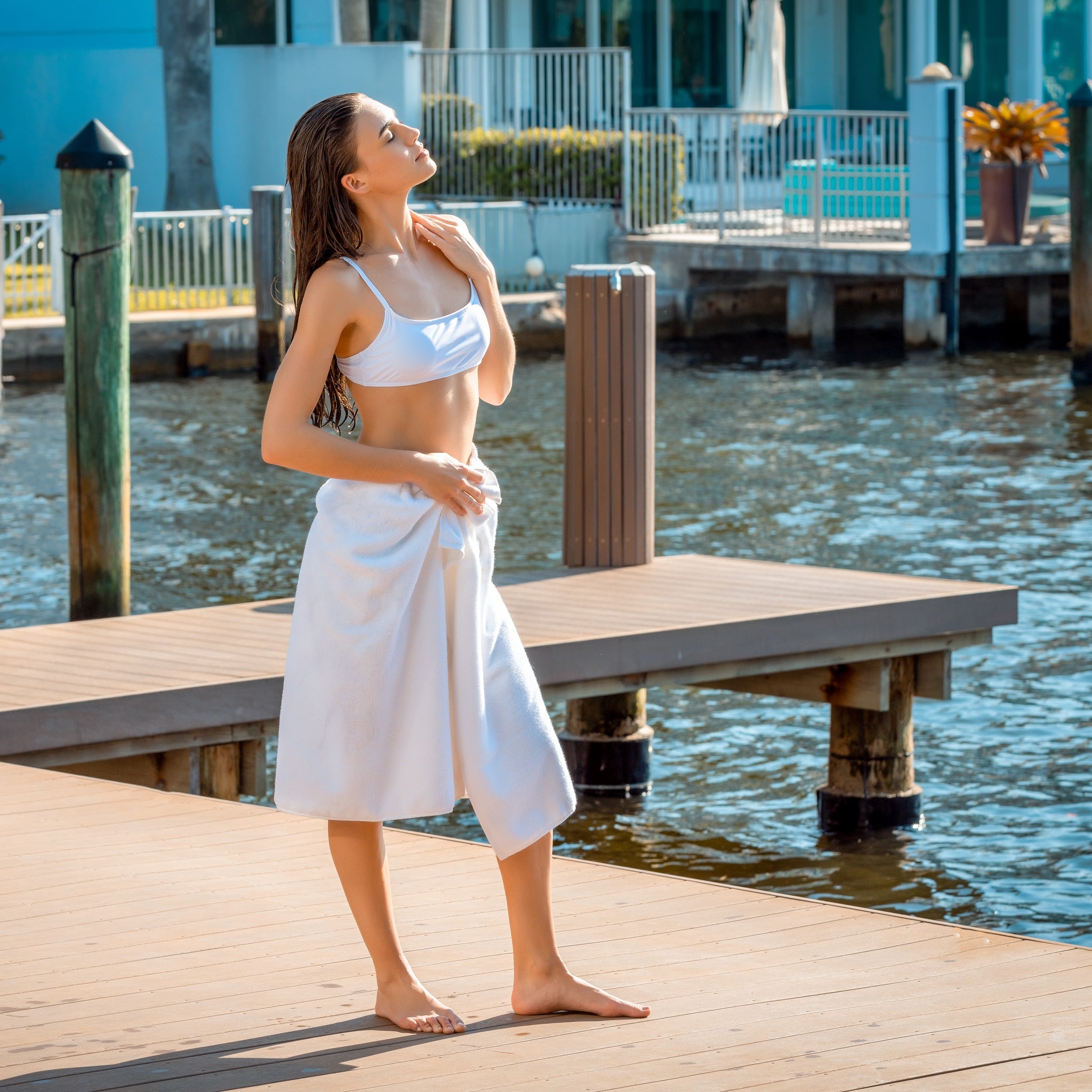 Woman in a white bikini and towel standing on a dock by water